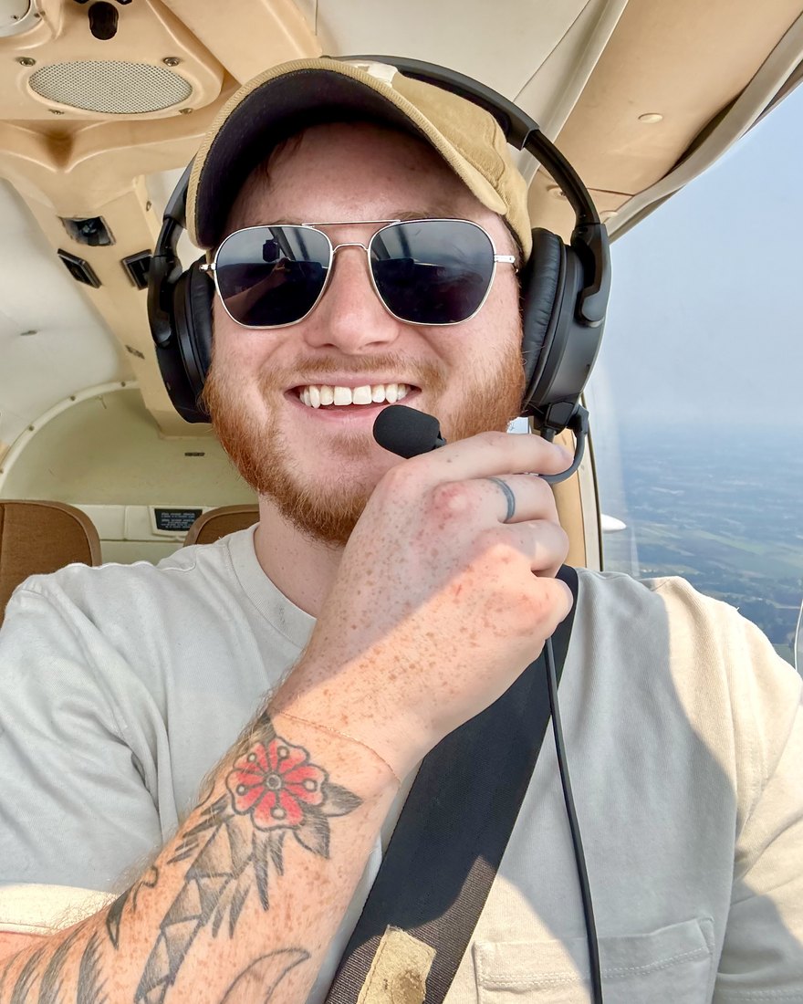 Logan Powers in the cockpit, smiling in a headset and cap